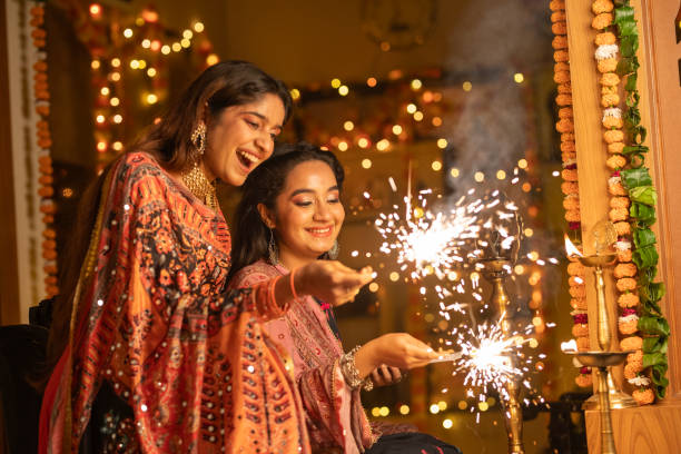 Cheerful beautiful sisters playing with sparklers while celebrating Diwali festival together at illuminated home